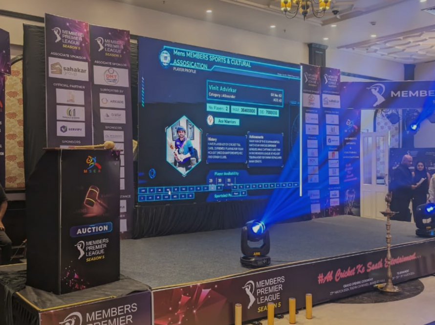 Stage set up for Cricket Premier League with spotlight and cricketer's name on the presentation screen, in side a banquet hall