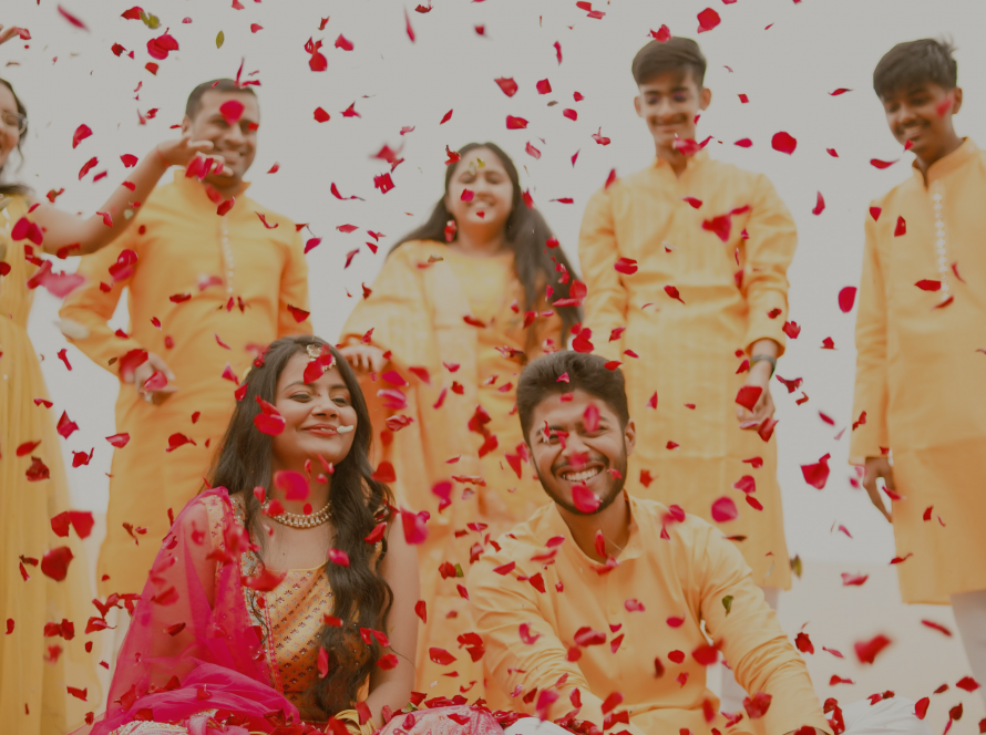 Bride and Groom Sitting in the center being showered with flowers by friends and family surrounding them on their haldi ceremony