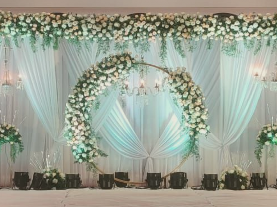 Reception stage decor with white back drop and white flowers decorated in a giant circle at the center