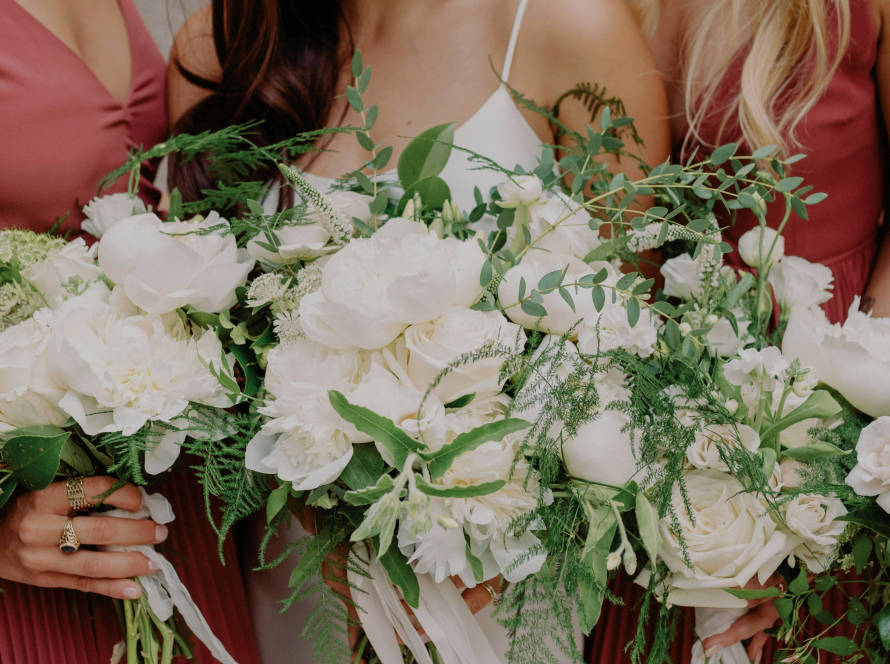 3 bridesmaid surrounding the bride holding white flower bouquet